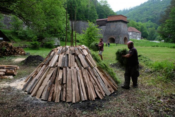 Stará huť u Adamova, květen 2024, stavba milíře - pokrývání vrstvou trávy oddělující dřevo od mourového pláště